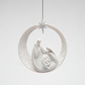 A white ceramic Christmas ornament depicting the Holy Family inside a crescent moon with a star at the top, hanging against a light gray background.