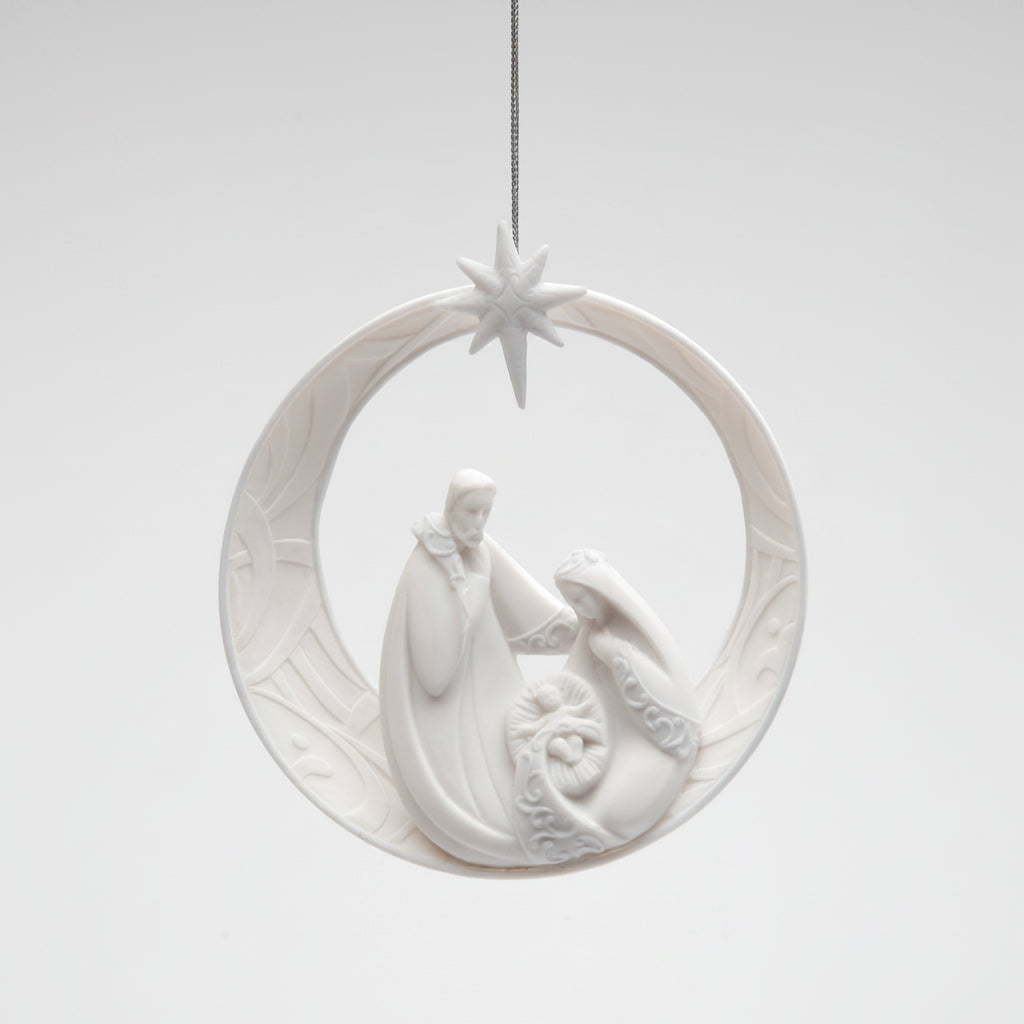 A white ceramic Christmas ornament depicting the Holy Family inside a crescent moon with a star at the top, hanging against a light gray background.